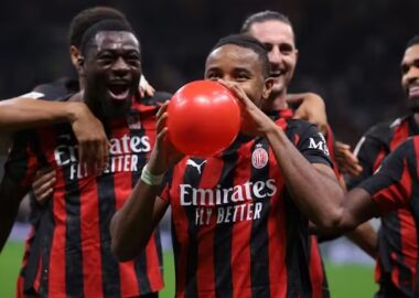 Pemain AC Milan, termasuk Ismaël Bennacer (kiri), Samuel Chukwueze (tengah) memegang dan meniup balon merah, merayakan gol di lapangan dengan rekan tim lain di belakang.