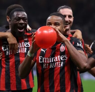 Pemain AC Milan, termasuk Ismaël Bennacer (kiri), Samuel Chukwueze (tengah) memegang dan meniup balon merah, merayakan gol di lapangan dengan rekan tim lain di belakang.