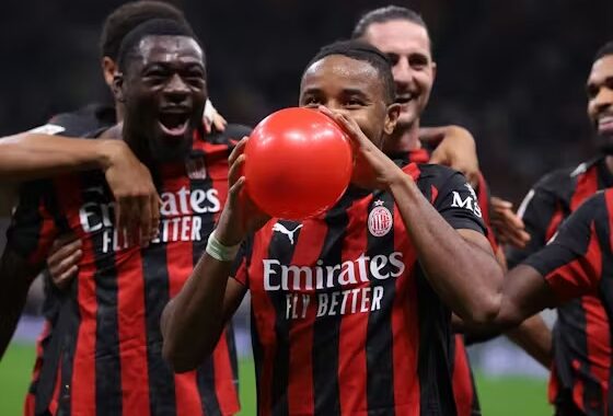 Pemain AC Milan, termasuk Ismaël Bennacer (kiri), Samuel Chukwueze (tengah) memegang dan meniup balon merah, merayakan gol di lapangan dengan rekan tim lain di belakang.