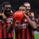 Pemain AC Milan, termasuk Ismaël Bennacer (kiri), Samuel Chukwueze (tengah) memegang dan meniup balon merah, merayakan gol di lapangan dengan rekan tim lain di belakang.